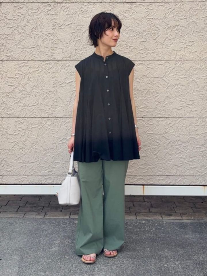 黒ブラウスとカーキパンツの女性が白いバッグを持ち横を向く
