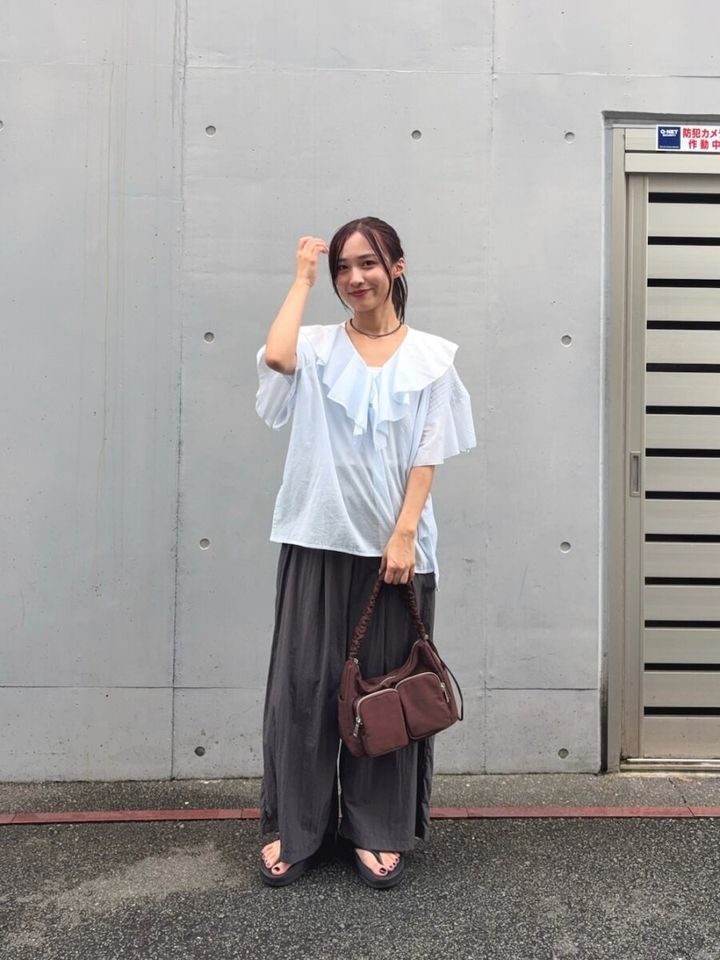 水色フリルブラウスとグレーパンツの女性が髪に手を添える