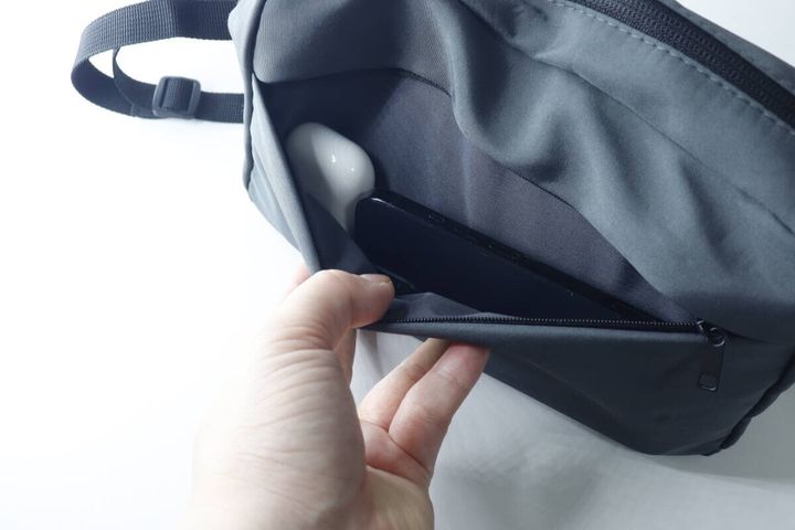 手がショルダーバッグのフロントポケットからスマートフォンとワイヤレスイヤホンを取り出している