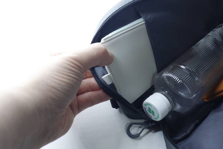 手が縦向きに持ったバッグの内ポケットから白い手帳を取り出している
