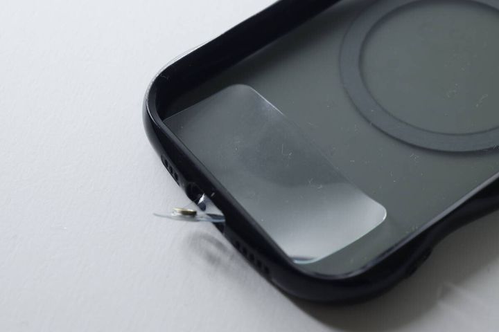 黒いスマホケースに透明なストラップホルダーを挟む様子