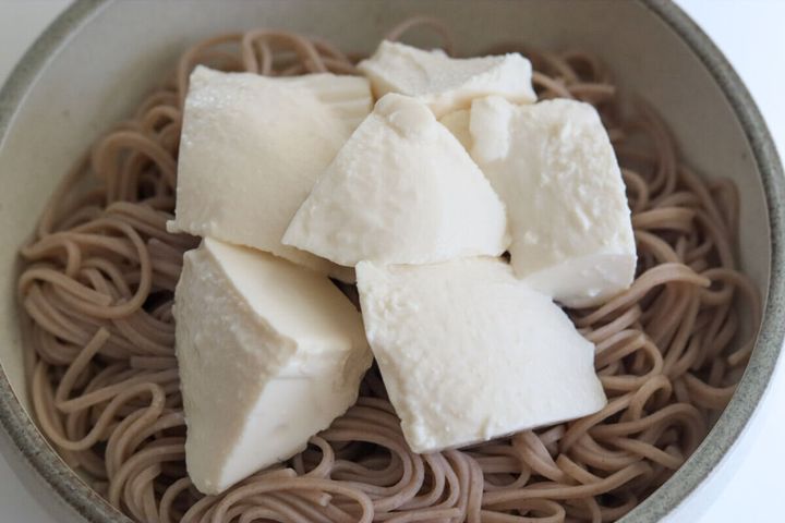 そばの上に大きく崩してのせられた白い絹ごし豆腐
