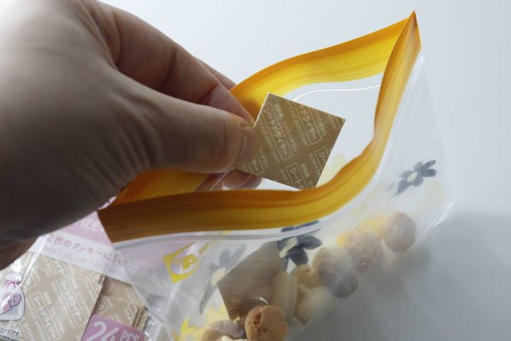 手がジップバッグにマカロンとシート乾燥剤を入れている様子