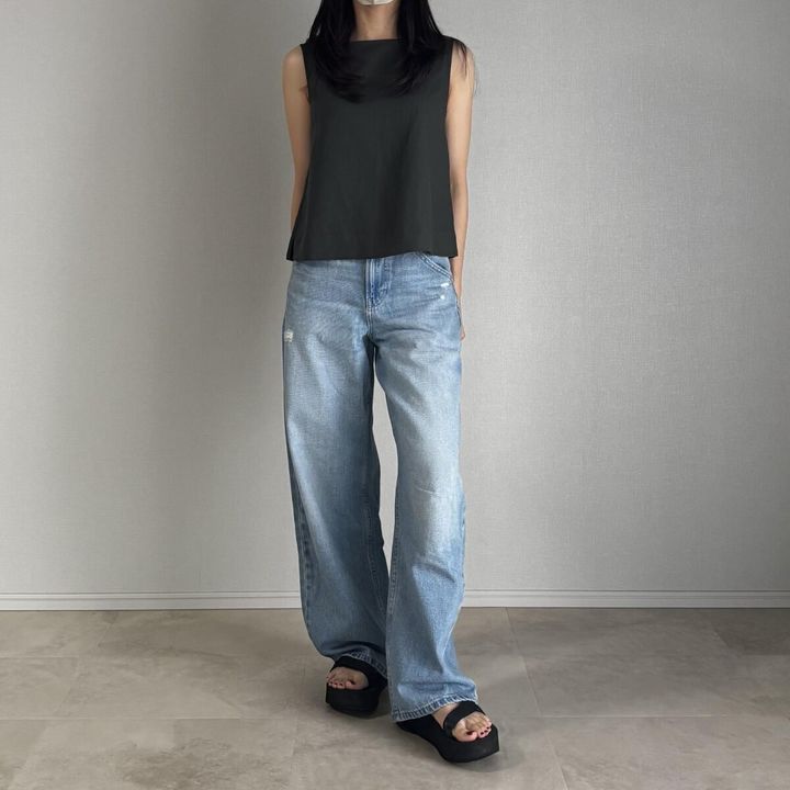 ダークグリーンのブラウスとダメージ加工のブルーデニムを着用した女性