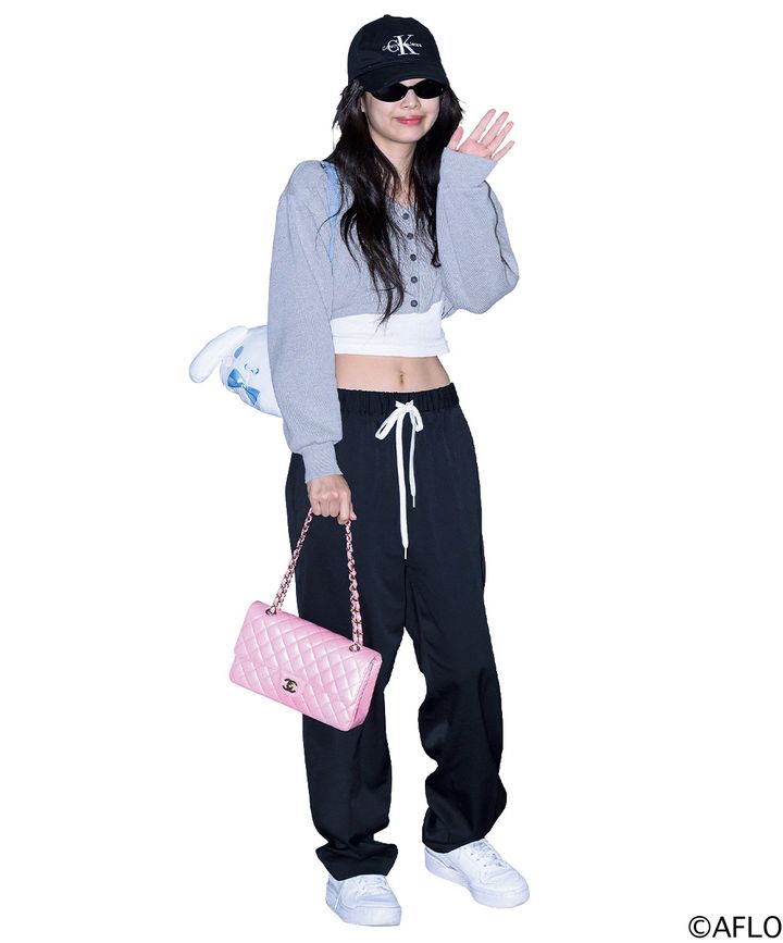 空港で手を振るBLACKPINKのジェニー。Calvin Kleinの黒いキャップとサングラスを着用し、グレーのショート丈カーディガンから綺麗に引き締まったウエストを披露。ドローストリング付きの黒いルーズパンツに、シャネルのピンクのチェーンバッグを合わせた私服スナップ。