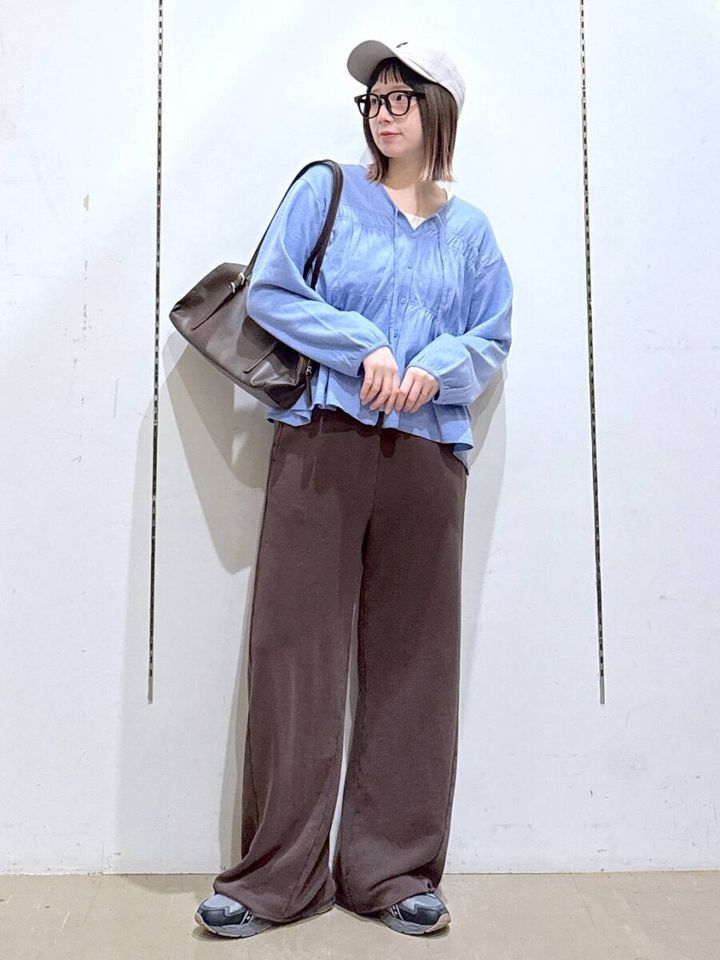 水色のシャーリングニットを着た女性がキャップとメガネで立つ