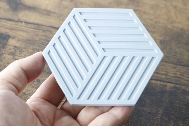 手のひらに乗せた淡いグレーの六角形シリコーンコースター