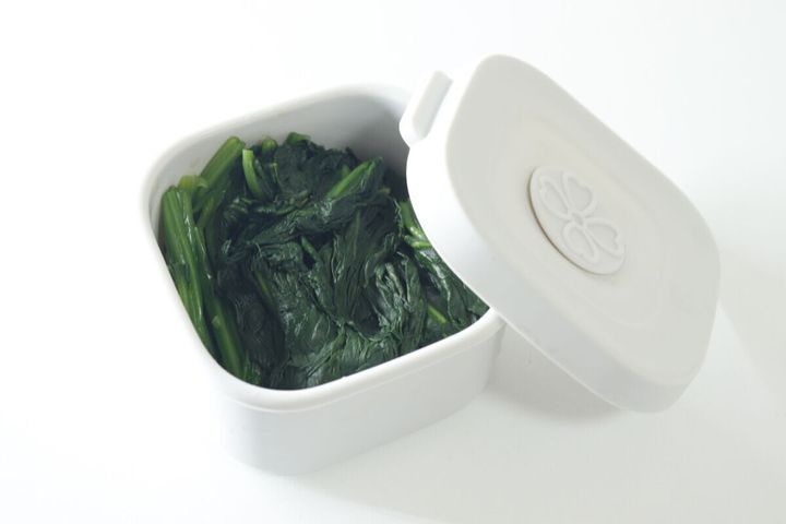 白い保存容器に茹でたほうれん草が入り、蓋が横に置かれている