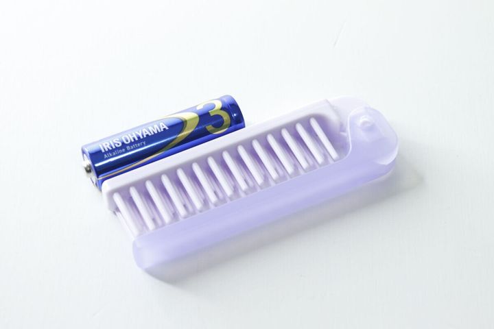 単3形乾電池と並べられた紫色の折りたたみヘアブラシ