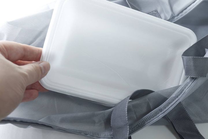 グレーの洗濯バッグに白い食品トレーを入れる手元