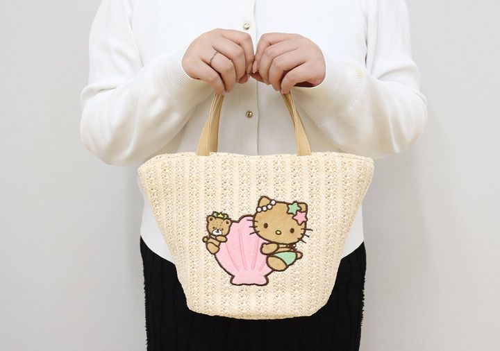 白い服を着た女性が日焼けハローキティのかごバッグを持っている