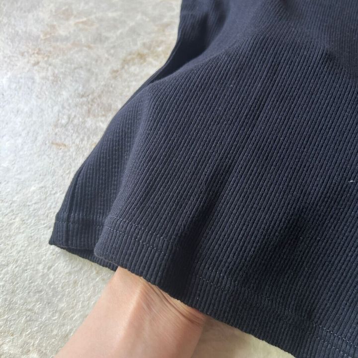 黒いリブミニTシャツの裾部分を指でつまんで生地のアップを見せている
