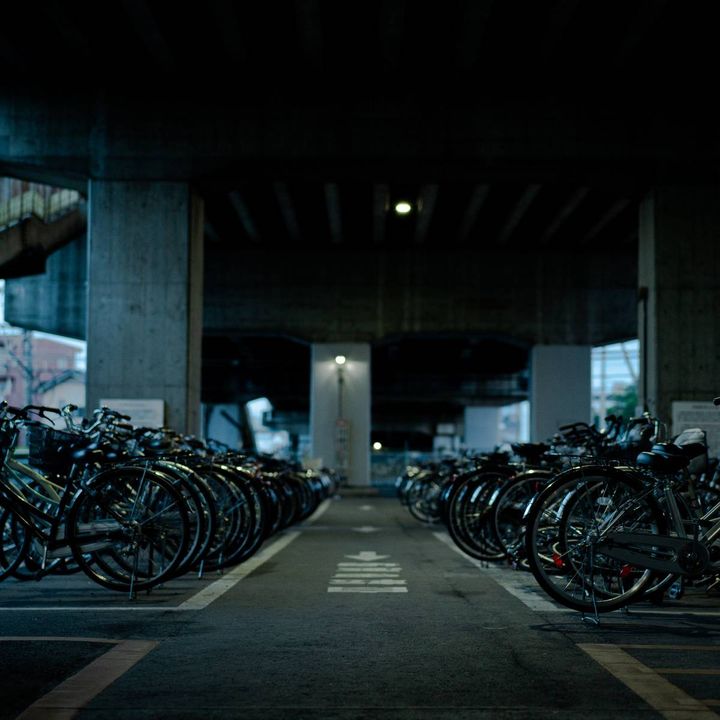 高架下に自転車が並ぶ、薄暗い夜の駐輪場