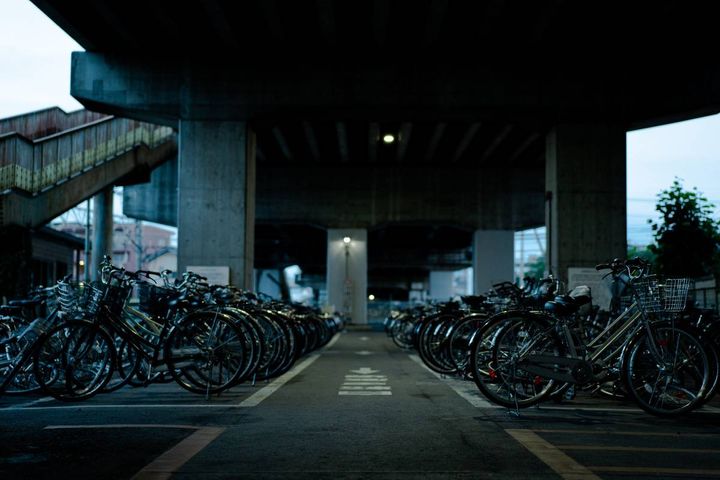 高架下に自転車が並ぶ、薄暗い夜の駐輪場