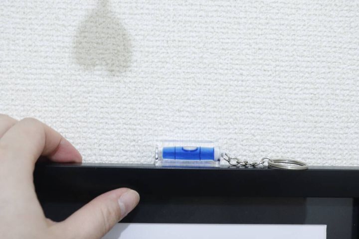 額縁の縁に置かれたキーホルダー水平器と手を添えている