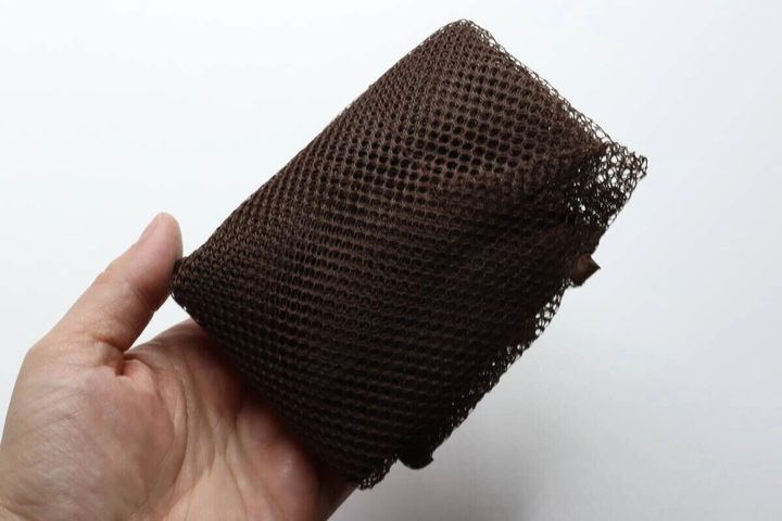 女性の手のひらに乗った、コンパクトに折りたたまれた茶色のメッシュバッグ