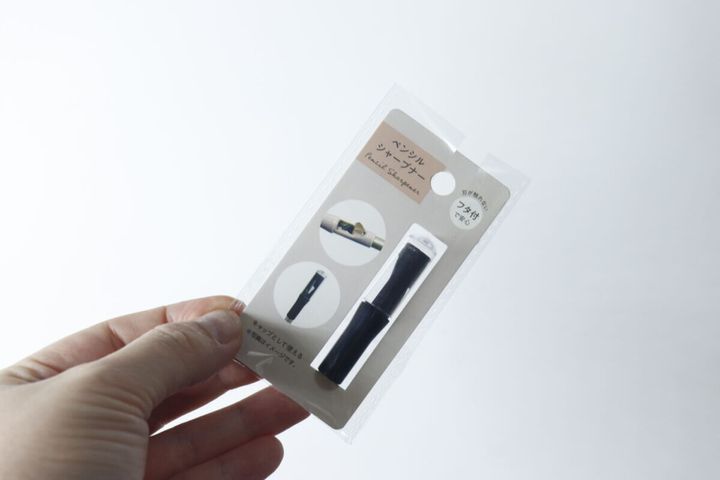 指で持ったセリアの「ペンシルシャープナー フタ付」商品パッケージ