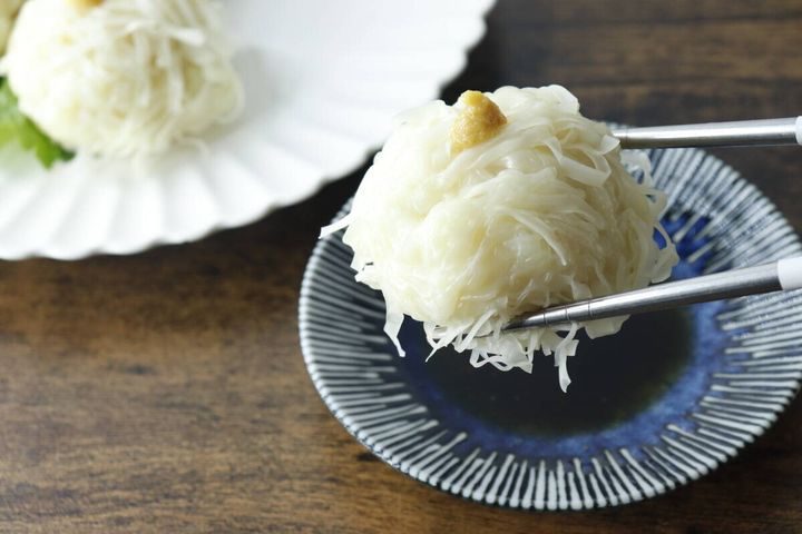 青釉たれ皿に盛り付けられた焼売を箸でつまんでいる