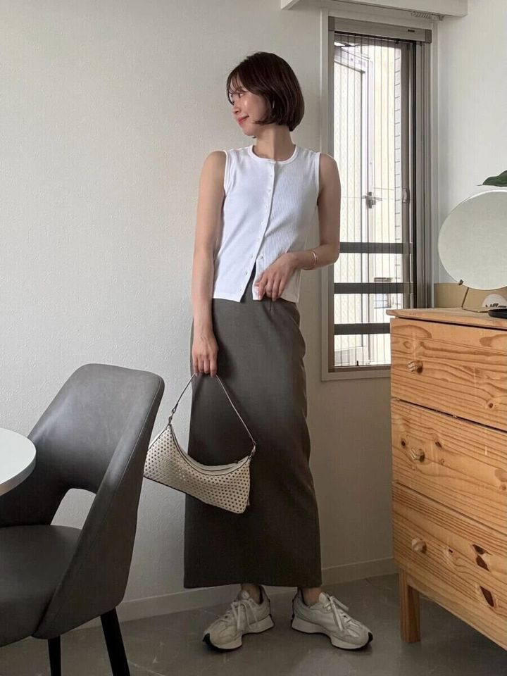白いノースリーブとカーキのIラインスカートを着用し、白いバッグを持つ女性の全身