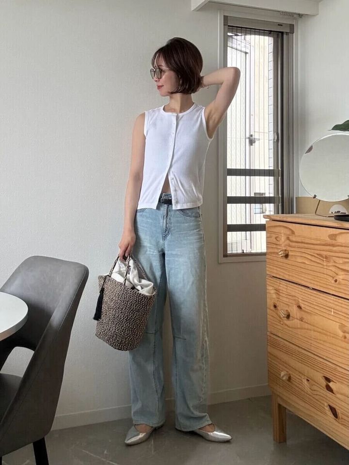 白いノースリーブと薄いブルーのワイドデニムを着用し、かごバッグを持つ女性の全身