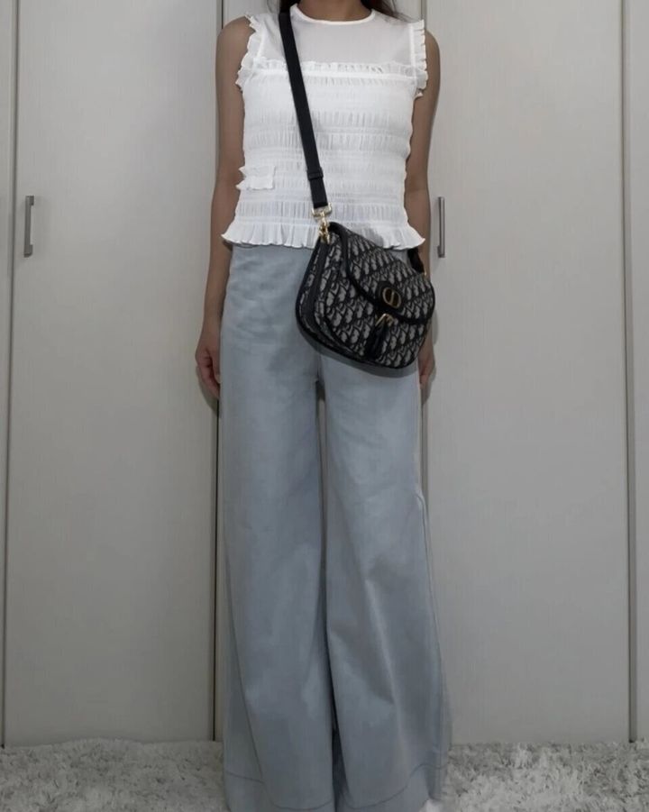 白いシャーリングノースリーブと薄いブルーのワイドデニムを着用した女性の全身