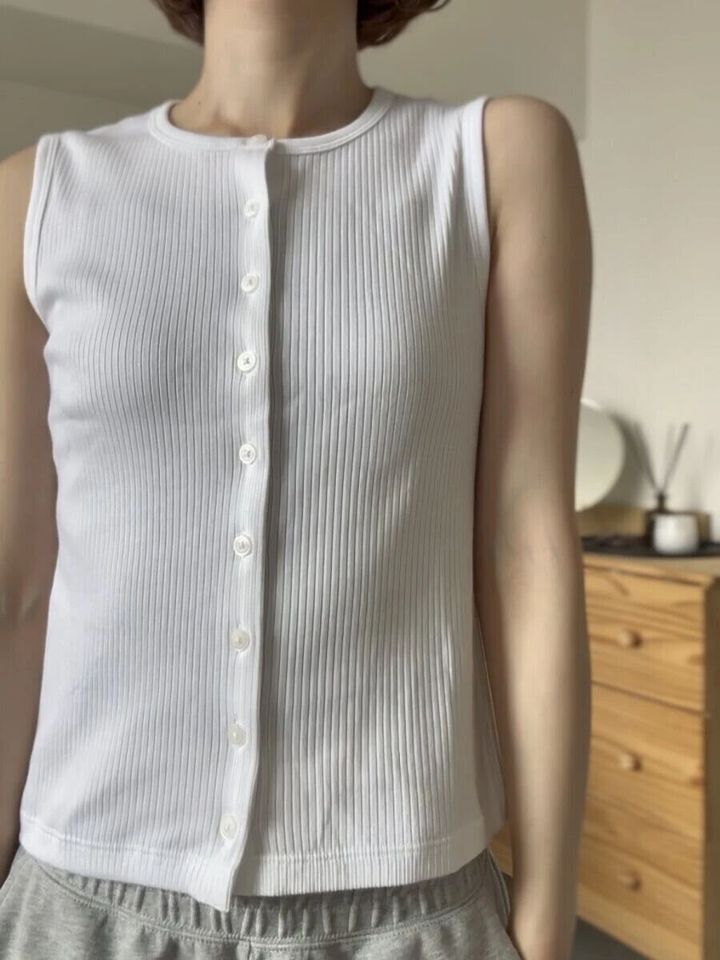 白いリブ素材のフロントボタンノースリーブトップスを着用した女性の胸元アップ