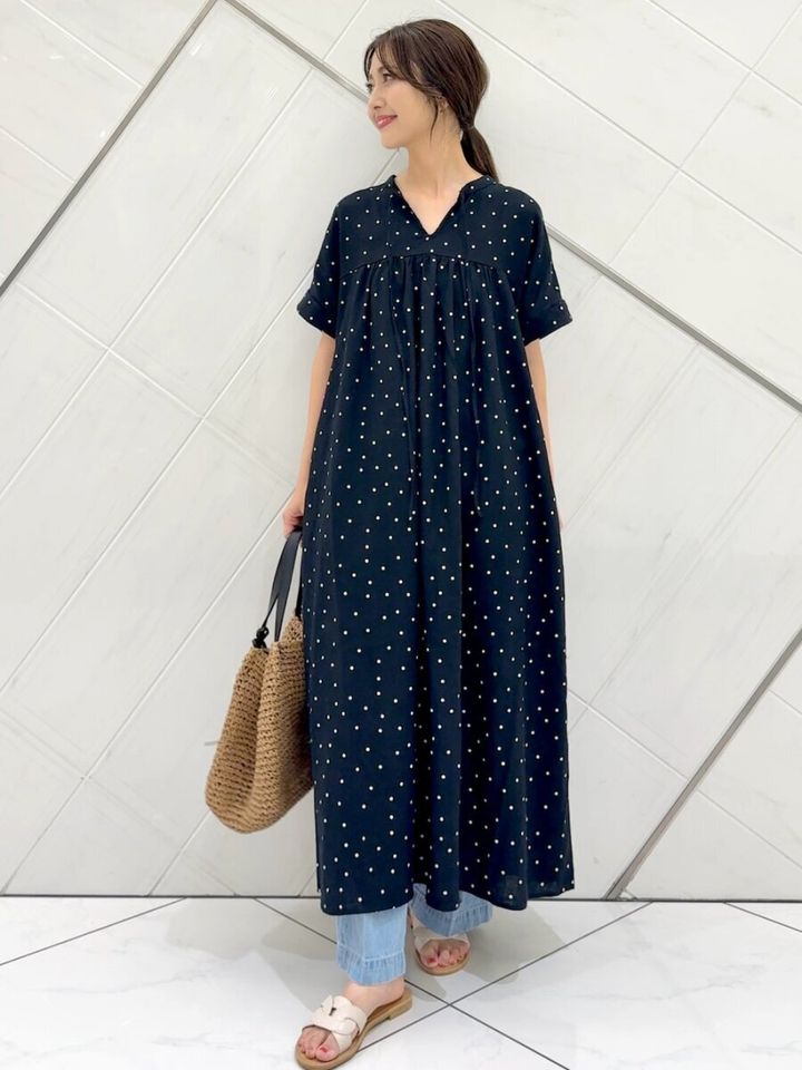 ドット柄黒ワンピースとデニムを重ね着し、かごバッグを持つ女性