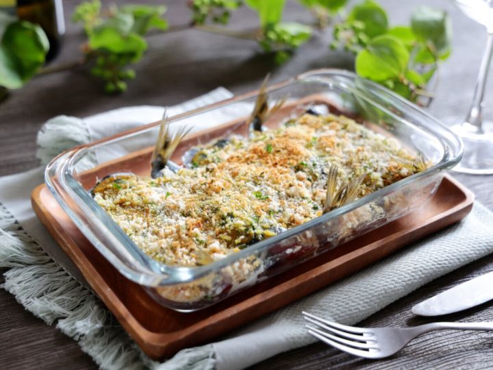 木製のトレイに乗ったガラス製の耐熱皿に入った、焼き上がったいわしとトマトのパン粉焼き