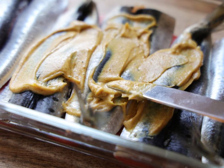 耐熱容器に並べられたいわしの皮目に、カレーマヨソースをスパチュラで塗っている様子