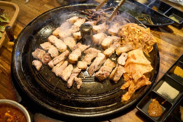 「サムギョプサル」W1万8000。薪火で焼くので香ばしく弾力満点。カレー塩やワサビで味変も楽しめる。ケランチムがセットでつく