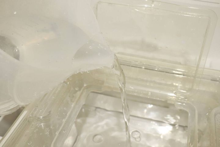 計量カップからウォーターサーバーのタンクへ水を注いでいる様子