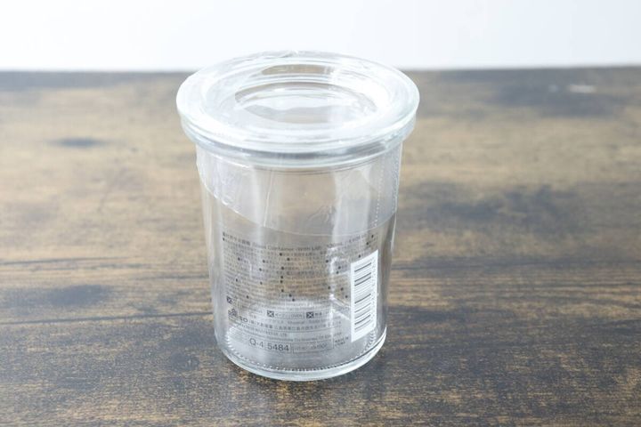 木目のテーブルに置かれた透明なガラス容器。側面には商品情報シールが貼られている。