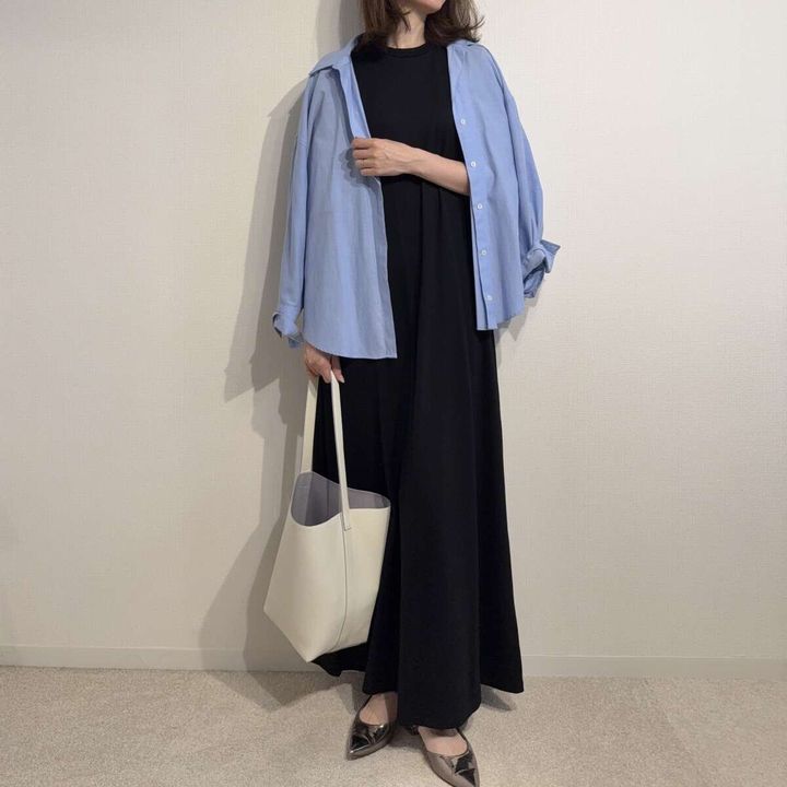 黒いワンピースに水色のシャツと白いバッグを合わせた女性の全身
