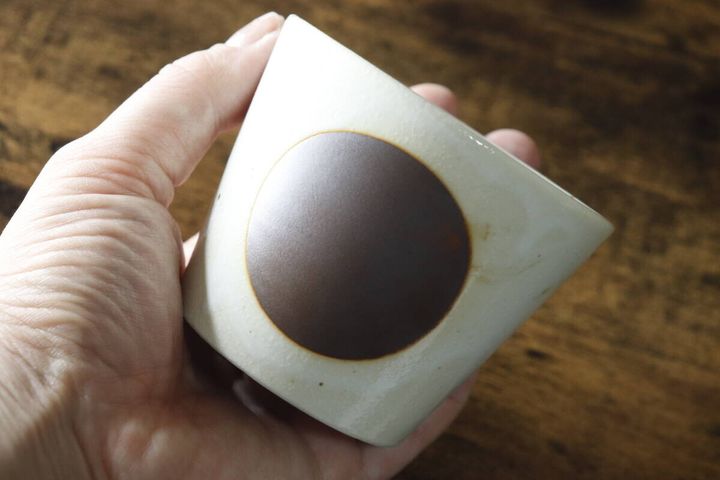 白地に茶色の丸紋があるそばちょこを手に持っている