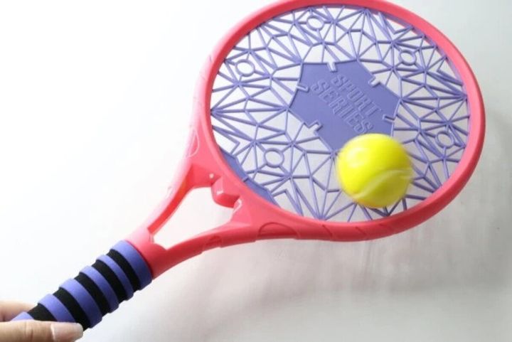 ピンク色のテニスラケットの網部分に黄色のボールが乗っている