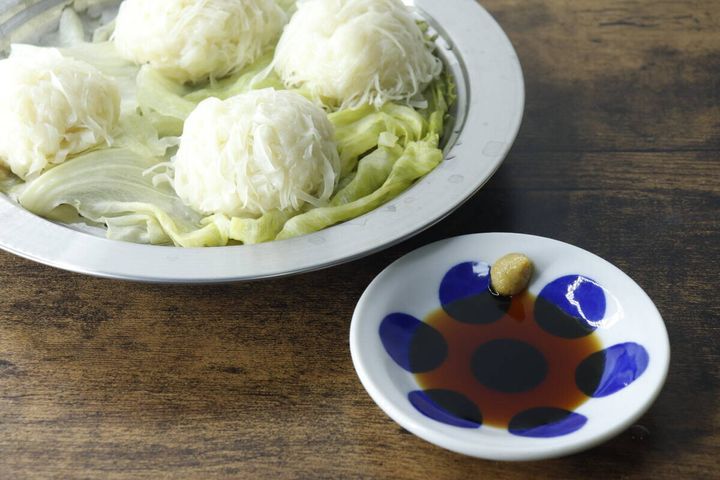 白い水玉模様の豆皿に醤油とからしが盛られ、奥に白い麺料理が置かれている