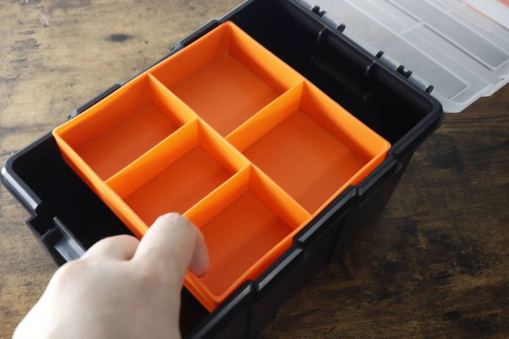 黒い工具箱の中のオレンジ色のトレーを、右手がスライドさせている