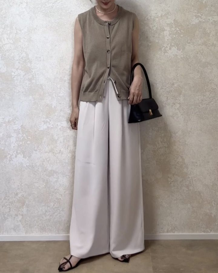 ベージュのノースリーブカーディガンと白いワイドパンツを着用した女性