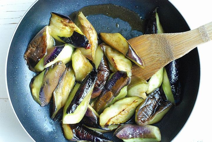 フライパンでなすを木べらで炒め、皮に焼き色がついている