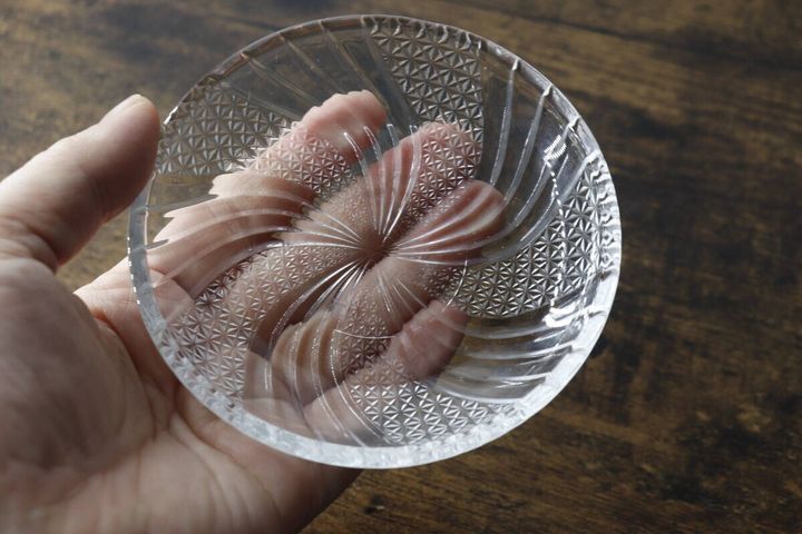 手のひらにガラス小皿を乗せ、光に透かして模様の美しさを確認している写真