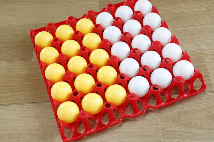 赤いボードの全ての穴に黄色と白色のピンポン玉がきれいに収まっている