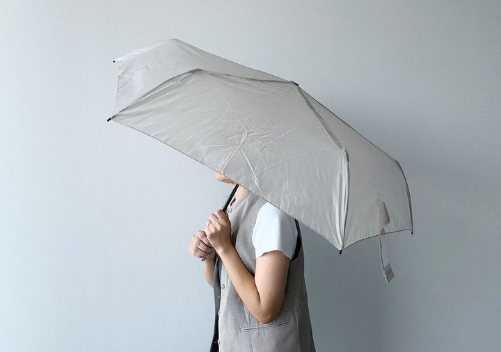 女性がベージュの折りたたみ傘を差している横顔