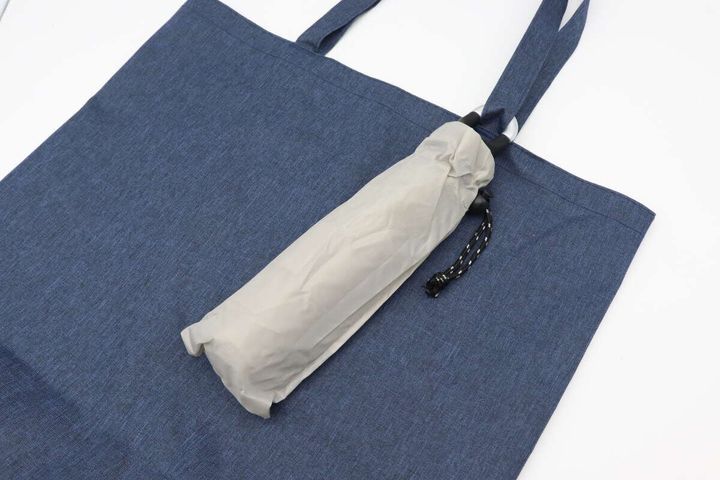 ベージュの折りたたみ傘が青いトートバッグの持ち手に取り付けられている様子