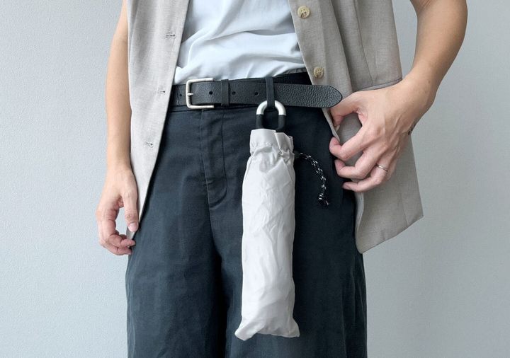 ベージュの折りたたみ傘が男性のベルトに吊り下げられている様子