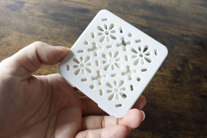 白い四角いカメムシよけ芳香剤本体を女性の手が持っている。表面には花柄の透かし模様がある