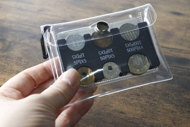 手が透明なポーチに入った硬貨入りのコインホルダーを持ち、中身が見えている