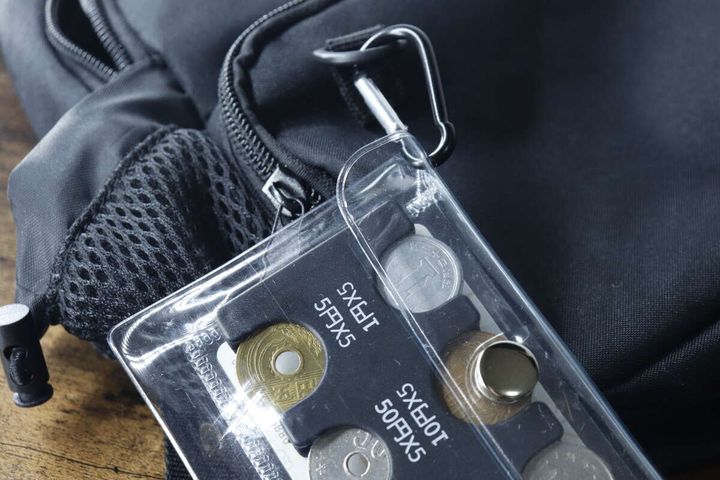 カラビナで黒いリュックサックのファスナー部分にポーチ付きコインホルダーが吊り下げられている