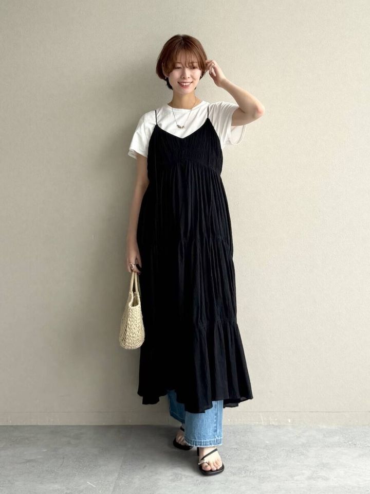黒キャミワンピと白T、デニムを重ね着した女性が笑顔で立つ