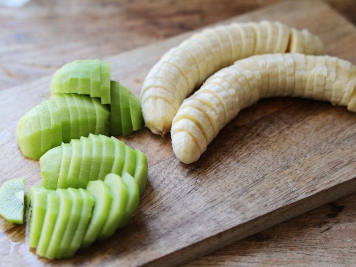 木のまな板の上に、皮をむいて輪切りにしたキウイとバナナが並べられている。