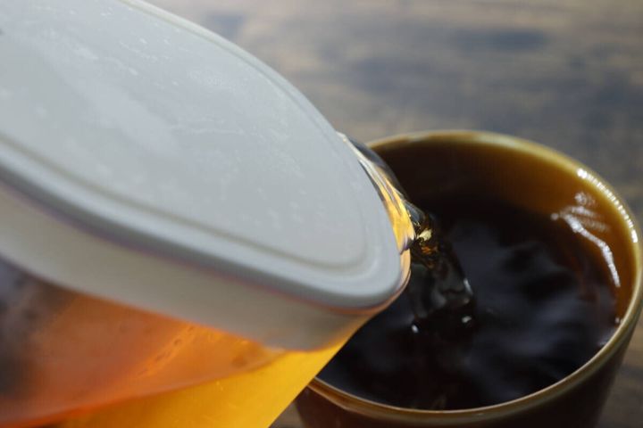 ピッチャーから茶色い飲み物をコップに注いでいる